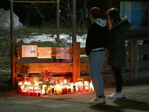 People stand beside layed candles and flowers on Via Aurina, in Lutago, South Tyrol, on January 5, 2020, at the location where a drunk driver ploughed into pedestrians killing six German tourists and injuring 11 other people.
