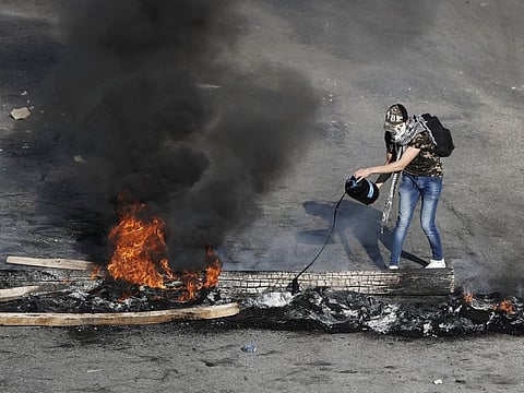 An anti-government protester drops oil on burning tires and wood during ongoing protests after weeks of calm in Beirut on Tuesday.