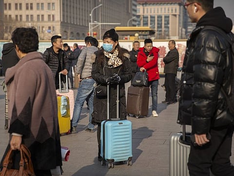 A traveler wears a facemask as she stands near the Beijing Railway Station in Beijing, Friday, Jan. 17, 2020. A second person has died from a new form of coronavirus in central China, health authorities said late Thursday. (AP Photo/Mark Schiefelbein)