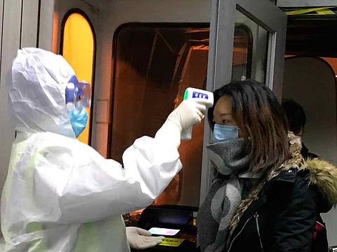 Health officials in hazmat suits check body temperatures of passengers arriving from the city of Wuhan at the airport in Beijing.