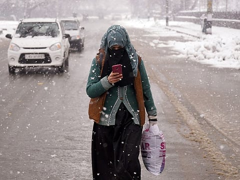 A girl using mobile phone walks on a road during fresh snowfall in Srinagar.