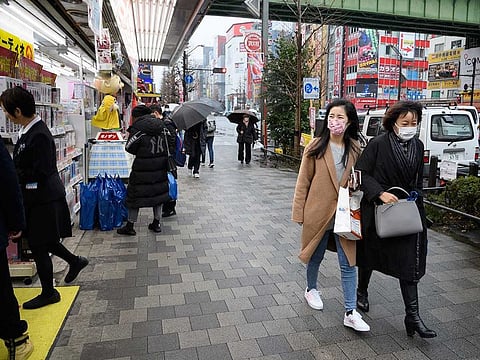 Visitors wearing face masks walk along a sidewalk in Tokyo's Akihabara area, Japan.