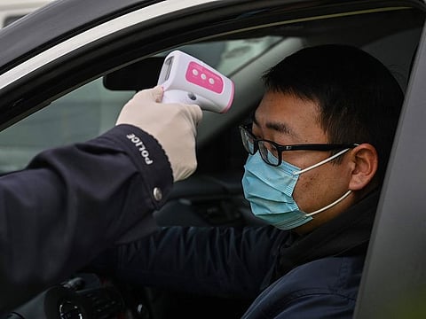 A police officer takes the temperature of a driver at a checkpoint on a street on the outskirts of Wuhan in China's central Hubei province on January 27, 2020, amid a deadly virus outbreak which began in the city. China on January 27 extended its biggest national holiday to buy time in the fight against a viral epidemic and neighbouring Mongolia closed its border, after the death toll spiked to 81 despite unprecedented quarantine measures.