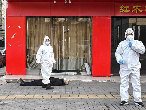 Officials in protective suits checking on an elderly man wearing a facemask who collapsed and died on a street near a hospital in Wuhan.