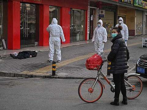 This photo taken on January 30, 2020 shows officials in protective suits checking on an elderly man wearing a facemask who collapsed and died on a street near a hospital in Wuhan.