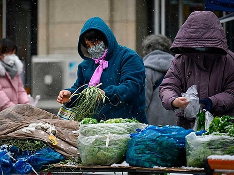 People wearing masks buy vegetables at a open market as snow falls in Beijing.