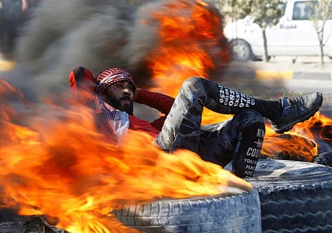 An Iraqi demonstrator sits amid burning tires blocking a road during ongoing anti-government protests in Najaf, Iraq February 2, 2020.