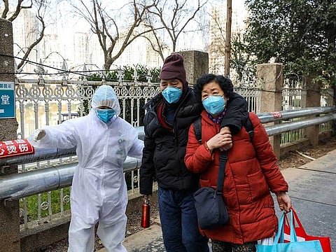A medical worker in a protective suit helps a couple outside a hospital in Wuhan in central China's Hubei Province.