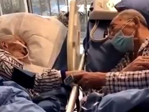 The video shows an elderly couple holding hands; both are in standard hospital beds