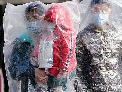 Passengers wearing masks and covered with plastic bags walk outside the Shanghai railway station in Shanghai, on February 9, 2020.