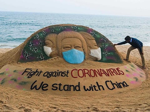 In this picture taken on February 10, 2020 Indian artist Sudarsan Pattnaik puts some final touches as he makes a sand sculpture depicting people wearing protective facemasks with a message reading 'Fight against coronavirus, We stand with China' at Puri beach in Puri.