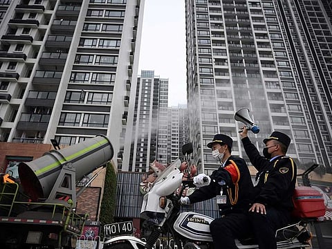 A man holding a loudspeaker sits on a motorcycle as it travels past a sanitizing vehicle disinfecting the public space near residential buildings, following an outbreak of the novel coronavirus in the country, in Panyu district of Guangzhou, Guangdong province, China February 11, 2020.