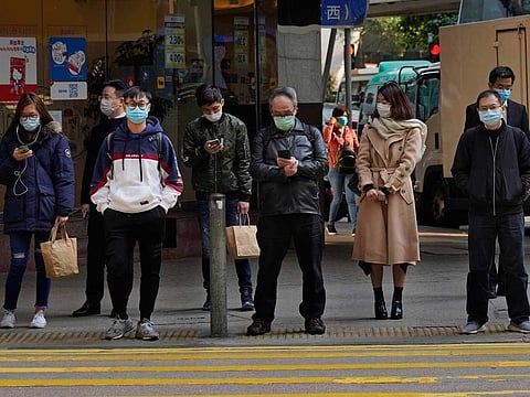 People wearing face mask stand at a downtown street in Hong Kong. A delayed travel bubble between it and Singapore will begin on May 26.