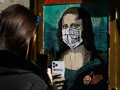 A woman takes a picture with her mobile phone of a poster by Italian urban artist Salvatore Benintende aka "TVBOY" depecting Leonardo da Vinci's Mona Lisa wearing a protective facemask and holding a mobile phone reading "Mobile World Virus" in a street of Barcelona on February 18, 2020, a week after the World Mobile Congress was cancelled due to fears stemming from the coronavirus that sparked an exodus of industry heavyweights.