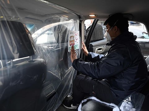 A worker installs a sticker reminding people about the COVID-19 coronavirus on a plastic sheet separating the driver and passenger compartments in a car at a disinfection station for Chinese ride hailing company Didi, in Beijing on February 24, 2020. The company is supplying drivers with masks and ordering them to disinfect their cars every four hours, as preventive measures against the COVID-19 coronavirus. / AFP / GREG BAKER