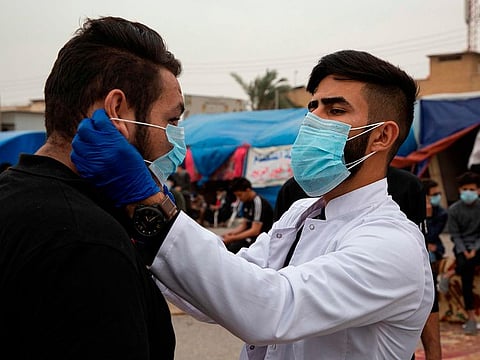 An Iraqi student shows an anti-government demonstrator how to wear a protective mask against the coronavirus during a rally in the southern Iraqi city of Basra on February 25, 2020. Iraq on February 24 confirmed its first novel coronavirus case in an elderly Iranian national in Najaf, according to health officials. A country with a dilapidated healthcare system, Iraq often hosts pilgrims and religious students from Iran, where at least a dozen people have died of the novel coronavirus since an outbreak there was first reported last week. Iraq had blocked travel to and from the Islamic republic days before announcing a seminary student in Najaf was the country's first confirmed case