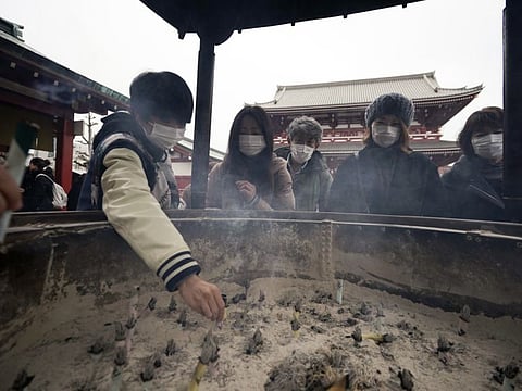 People with protective masks gather around a huge incense burner as they offer their prayers in the Asakusa district on Wednesday in Tokyo.