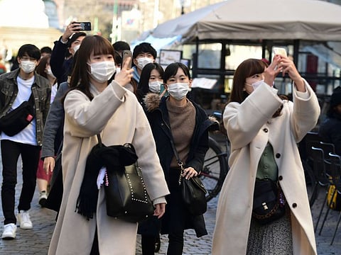 Tourists wearing protective face masks take pictures on Friday in the centre of Milan, after Covid-19, the novel coronavirus, spread to Italy.