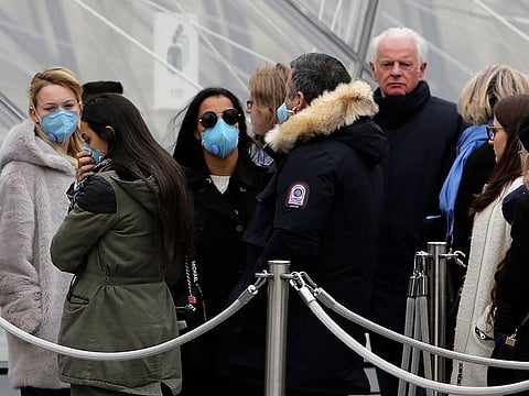 Tourists, some wearing a mask, queue to enter the Louvre museum Friday, Feb. 28, 2020 in Paris.