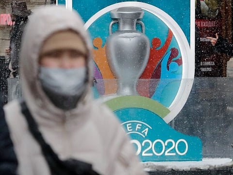 A person wearing a protective face mask walks past the Euro 2020 countdown clock in central Saint Petersburg, Russia.