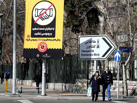 Iranians wearing protective masks walk under a prevention campaign poster for coronavirus on March 4 in Tehran.