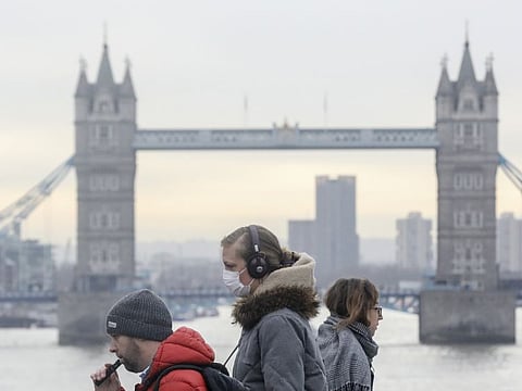 Commuters, including one wearing a protective face mask, walk over London Bridge, in view of Tower Bridge, in London on Wednesday.