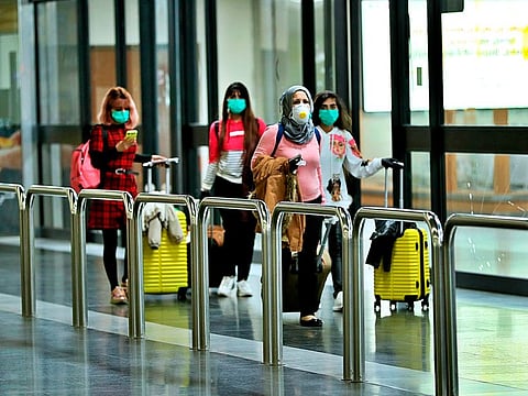 Passengers wearing protective masks walk with their belongings in Baghdad Airport, Iraq, Wednesday, March 4, 2020.