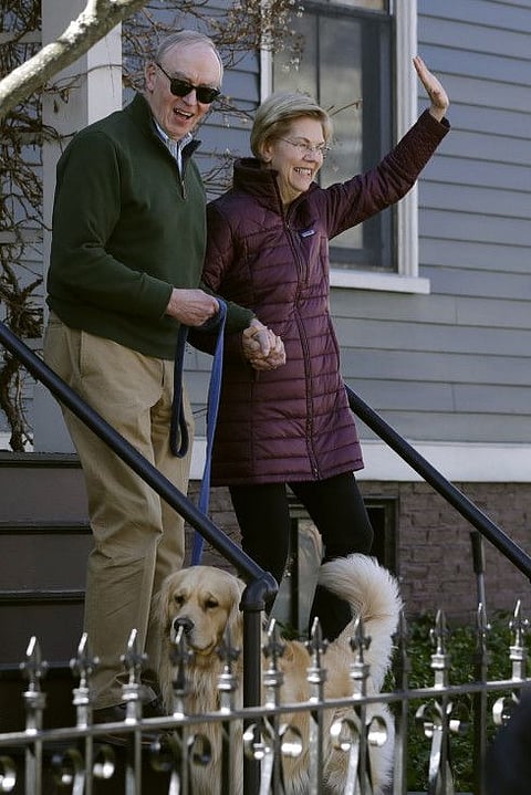 Elizabeth Warren, with her husband Bruce Mann and dog Bailey, greets media outside her home on Thursday.