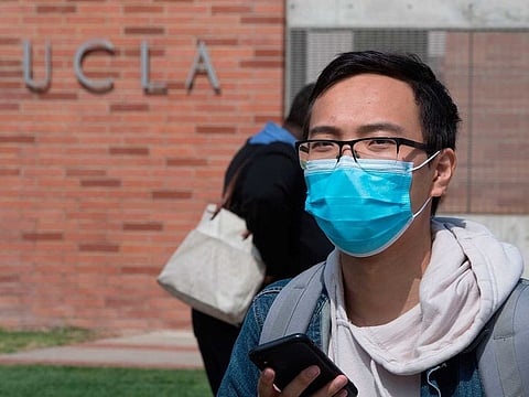 A student wears a face mask to protect against the COVID-19 (Coronavirus) as he leaves the campus of the UCLA college in Westwood, California