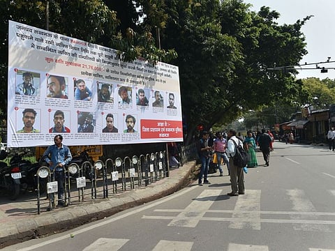 People walk past a poster displaying photographs of those who have been identified to pay compensation for vandalising public property during protests against the Citizenship Amendment Act, in Lucknow, on March 6, 2020.
