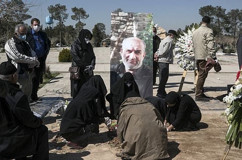 Relatives wearing face masks mourn over the grave of former politburo official in the Revolutionary Guard Farzad Tazari, shown in poster, who died Monday after being infected with the new coronavirus, at the Behesht-e-Zahra cemetery just outside Tehran on Tuesday.