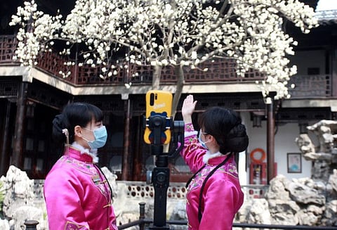 Tour guides wearing face masks show a blooming flower tree through a live-streaming platform, at a closed tourist attraction following the novel coronavirus outbreak in the country, in Yangzhou, Jiangsu province, China on March 11, 2020.