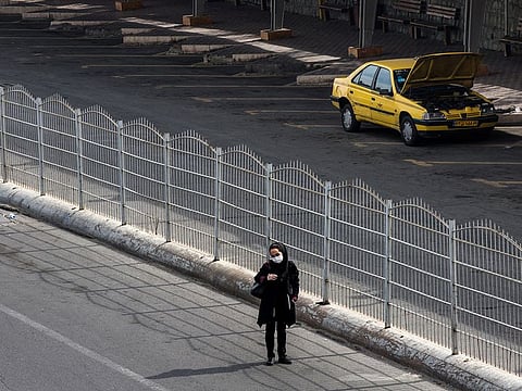 A woman waits for a taxi at an empty taxi in Tehran, Iran, Friday, March 13, 2020. Iran is scrambling to control one of the worst outbreaks of the coronavirus in the world.