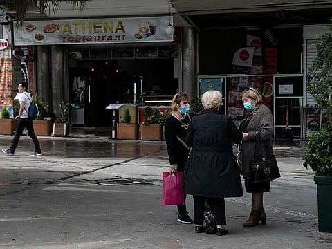 Women wearing protective masks chat at a central square, in Athens, Sunday, March 15, 2020.