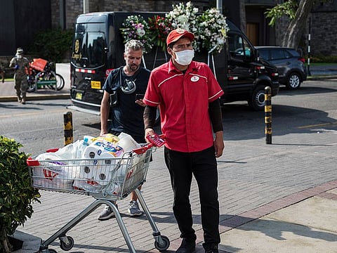 A supermarket worker, wearing a face mask as a precaution against the new coronavirus, stands next to a full cart before loading the purchase into a client’s car, in Lima, Peru, Monday, March 16, 2020.