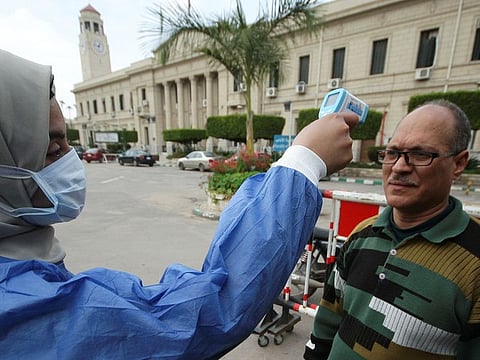 A medical staff member in protective gear checks the temperature of a university employee amid concerns over the coronavirus (COVID-19), following the suspension of study for only undergraduate students at Cairo University to prevent it spreading, in Cairo