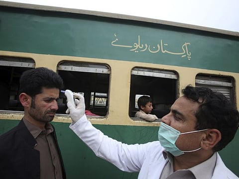 A Pakistani volunteer checks the body temperature of passengers arriving at a railway station in Peshawar, Pakistan on March 17.