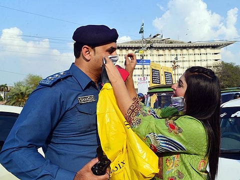 An activist of Sweet Sixteen group offering a mask to a traffic warden at the Mall Road in Lahore on Wednesday. Pakistan has imposed harsh travel restrictions for passengers travelling to the country to prevent coronavirus spread.