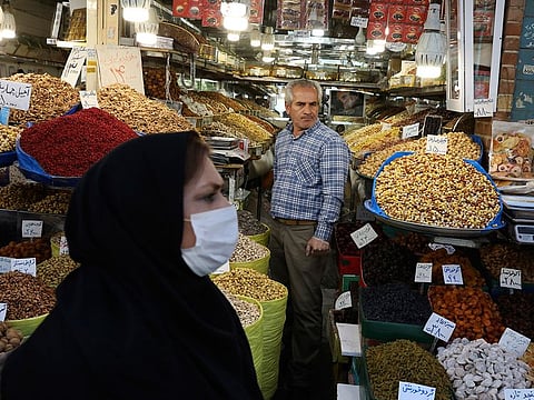 A shopkeeper waits for customers as a woman wearing a face mask to help protect against the new coronavirus, walks at the Tehran's Grand Bazaar, Iran.