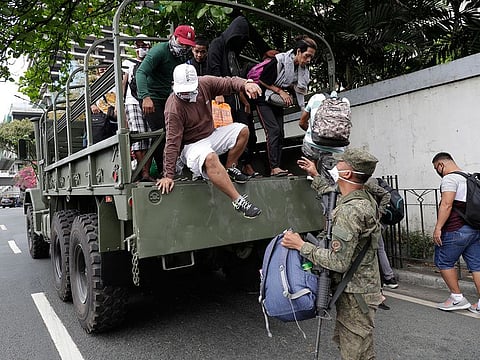 Commuters go down a military truck as they offer a free ride after public transportation have been halted due to the enhanced community quarantine to prevent the spread of the new coronavirus along an almost empty hi-way in Manila, Philippines.