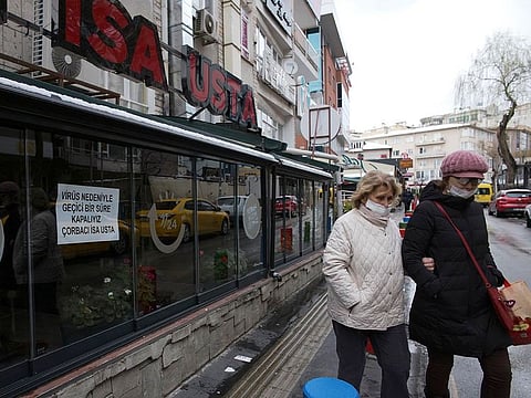 Face-masked people walk past closed restaurants, in Ankara, Turkey, Thursday, March 19, 2020.