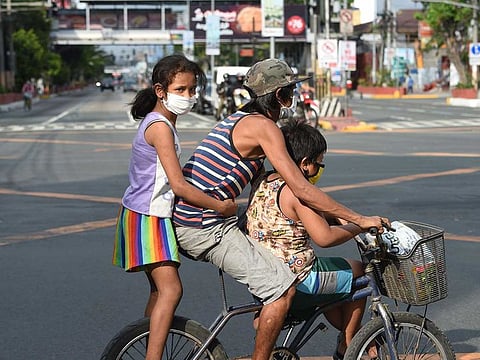 A father with his children rides a bicycle on an almost empty road in Manila on March 20, 2020, after the government imposed an enhanced community quarantine against the rising numbers of COVID-19 infections.
