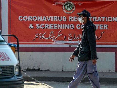 A resident wearing a facemask as a preventive measure against the COVID-19 coronavirus, walks past a banner at a coronavirus registration and screening counter at the Pakistan Institute of Medical Sciences Hospital in Islamabad on March 19, 2020.