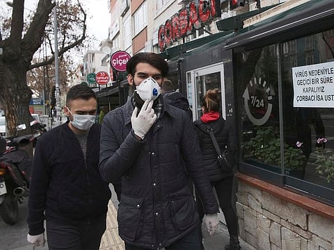 Men wearing protective masks walk past closed restaurants and cafes, in Ankara, Turkey, Friday, March 20, 2020.