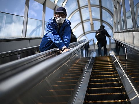 A staff wearing a face mask cleans an escalator in Sendai railway station on March 21, 2020.