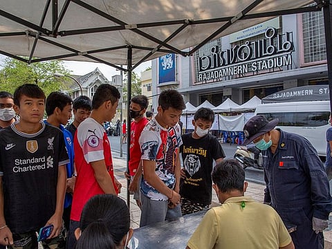 In this Thursday, March 19, 2020 photo, Muay Thai boxing fighters and officials gather at a makeshift screening facility outside Rajadamnern boxing stadium in Bangkok, Thailand.