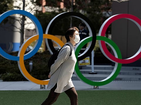 A woman walks with a protective face mask following the outbreak of coronavirus pandemic past the Olympic rings in front of the Olympics Museum in Tokyo.