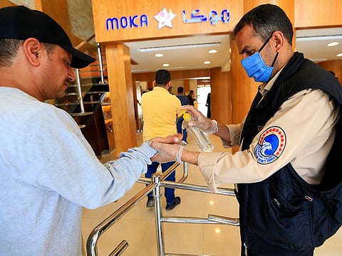 A security guard wearing a protective mask sprays sanitizer onto the hands of incoming customers as a measure against COVID-19 coronavirus disease, outside a coffee shop in Yemen's capital Sanaa