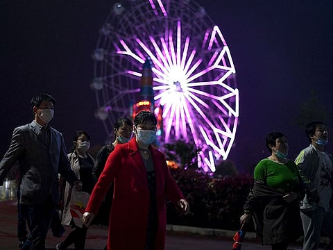 People wearing facemasks walk along a theme park, after a months-long lockdown as a preventive measure against the COVID-19 coronavirus, in Macheng in China’s central Hubei province on March 25, 2020.