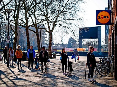 Shoppers observe social distancing as they wait in a queue outside a supermarket in Walthamstow, east London on March 27, 2020, after Britain's government ordered a lockdown to slow the spread of the novel coronavirus COVID-19.